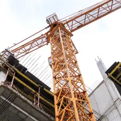 Pomarańczowy dźwig budowlany unosi się nad betonową konstrukcją. To właśnie dźwig pomaga wznosić kolejne piętra.