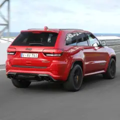 Czerwony Jeep Grand Cherokee Trackhawk SRT pędzi po torze wyścigowym, jego potężny silnik brzmi jak burza.