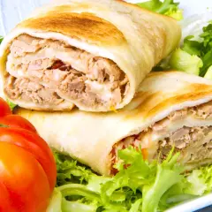 Dos rollos de wrap de atún, rellenos de atún desmenuzado y queso, servidos con lechuga fresca y tomates.