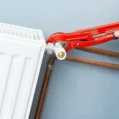 Mano con pinza rossa che lavora sulla valvola di un termosifone bianco, mostrando come smontare un termosifone.