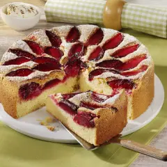 Szybkie ciasto ze śliwkami na oleju, posypane cukrem pudrem, z kawałkiem na łopatce. Obok miseczka bitej śmietany.