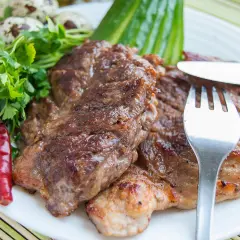 Saftiges Schweinesteak, mariniert und perfekt gegrillt, serviert mit Petersilie, Chilischoten und Wachteleiern. Ein Genuss für Fleischliebhaber.