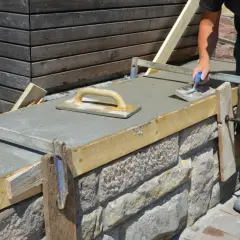 Arbeiter glättet frischen Beton auf einer **Wandschalung**. Der Aufbau der Schalung aus Holz und Metall ist gut sichtbar.