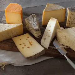 Assortiment de fromages, dont un beau morceau de comté pâte cuite, sur une planche en bois.