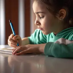 Ein Mädchen konzentriert sich auf das Nachspuren von Buchstaben in ihrem Heft, eine typische Übung für die Grundschule.