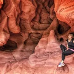 Una mujer sonríe sentada en las impresionantes formaciones rocosas de las coves de Can Riera, un paisaje natural de arenisca erosionada.