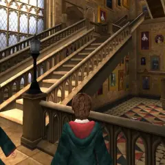 Dwóch uczniów w szatach Gryffindoru przemierza korytarz Hogwartu, jak w grach Harry Potter. Obok schodów wiszą ruchome portrety.