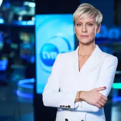 Kobieta w białej marynarce, prezenterka TVN Fakty, stoi na tle studia. Jej spojrzenie jest pewne, a postawa świadczy o profesjonalizmie.