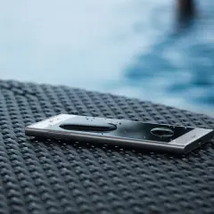 Smartfon z kroplami wody na ekranie, leżący na plecionej powierzchni. Dowód, że IP68 co oznacza: odporność na zanurzenie.
