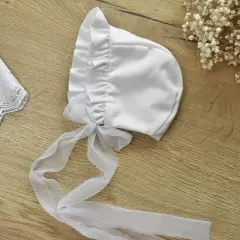 Elegancka, biała bonetka do chrztu z tiulową kokardką i koronkowym wykończeniem.