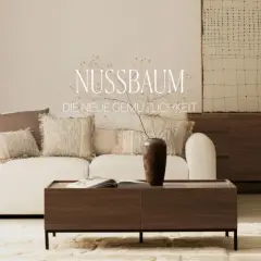 Gemütliches Wohnzimmer mit weißem Sofa, Kissen und einem Couchtisch aus dunklem Holz. Ein Sideboard aus dunklem Holz steht im Hintergrund.