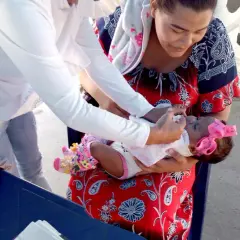 Kolumbia: matka trzyma dziecko, które otrzymuje szczepienia. Dziecko ma różową kokardkę na głowie.