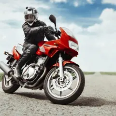 Motociclista con casco e giacca in pelle, in posizione di guida sportiva su una moto rossa su una strada vuota.