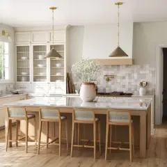 Jasna kuchnia w stylu modern classic z wyspą i czterema hokerami. Jasne drewno, złote detale i dużo światła tworzą przytulną atmosferę.