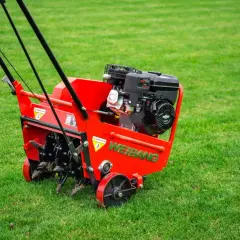 Czerwony aerator Weidemann na zielonej trawie. Idealny czas na aerację trawnika, gdy jest wilgotna i gotowa na odżywienie.