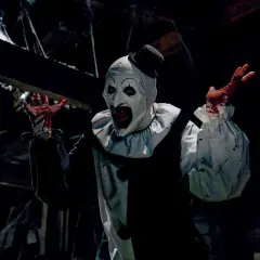 Krwawy klaun Art, znany z najbardziej krwawych horrorów, z rękami ubrudzonymi krwią, w mrocznym, pajęczynowym otoczeniu.