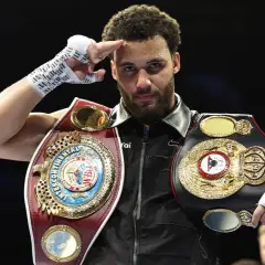 A boxer, champion of the super flyweight weight class, salutes with his championship belts.