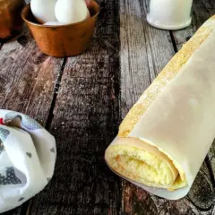 Rotolo di pasta biscotto perfetta, soffice e dorata, avvolta in carta forno. Ingredienti freschi in primo piano.