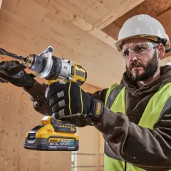 Budowlaniec w kasku i okularach wierci w drewnie najmocniejszą wkrętarką DeWalt. Wióry lecą w powietrzu.