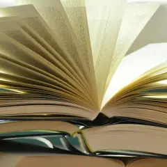 Otwarta książka na stosie innych. Różnica między romansem a literaturą obyczajową z wątkiem miłosnym jest jak między stronami tej książki – subtelna, lecz znacząca.