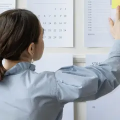 Kobieta planuje swój 4 dniowy tydzień pracy, przyczepiając notatki do tablicy.