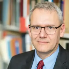 Porträt von Andreas Wirsching, der in einem Anzug und mit Brille vor einem Bücherregal steht.