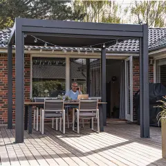 Man arbetar på laptop vid ett bord under en pergola, perfekt för att bygga uteplats. Ljusslinga ovanför.