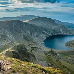 Vue panoramique d'un trek en Bulgarie. Des lacs glaciaires d'un bleu profond bordent des montagnes verdoyantes sous un ciel nuageux.