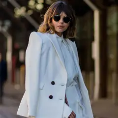 Mujer con traje blanco, gafas de sol redondas y cabello castaño. Su atuendo, elegante y sencillo, refleja el **minimalista significado** de la moda.