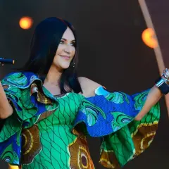 Kayah w kolorowej sukience z falbanami śpiewa na scenie, trzymając mikrofon.