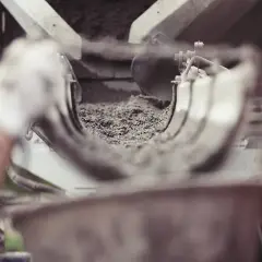 Ręka w białej rękawiczce wsypuje cement do maszyny.