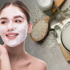 Mujer con mascarilla de arroz para la cara, junto a un cuenco con agua de arroz y granos de arroz.