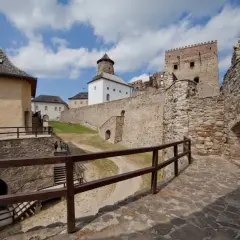 Kamienne mury i wieże zamku Stará Ľubovňa wznoszą się na tle błękitnego nieba z chmurami.