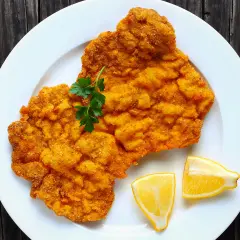 Ein knuspriges Schnitzel im Backofen, garniert mit Petersilie und Zitronenspalten, auf einem weißen Teller.