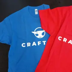 Niebieska i czerwona koszulka z logo "CRAFT-IT" i kowadłem. To przykład, jak sitodruk co to za technika, pozwala tworzyć trwałe nadruki na odzieży.