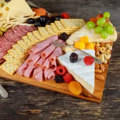Apetyczna deska wędlin na imprezę: sery, kiełbaski, szynka, oliwki, winogrona, owoce i orzechy.