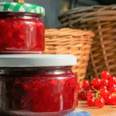 Słoiki z domowym dżemem z porzeczki czerwonej, obok świeże owoce. W tle plecione kosze.