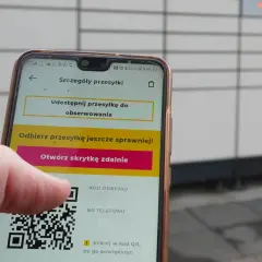 Dłoń trzyma smartfon z aplikacją InPost, wyświetlającą kod QR i opcję otwarcia skrytki.