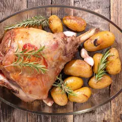 Gigot d'agneau rôti, doré et savoureux, accompagné de pommes de terre grenaille et d'ail, prêt pour la cuisson.