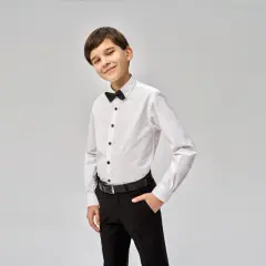 Chłopiec w eleganckiej białej koszuli z czarną muszką i spodniach. Idealny strój, co na komunie dla chłopca.