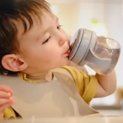Un petit garçon boit de l'eau dans une tasse à bec, assurant son hydratation bébé.