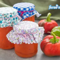 Barattoli di pesto di peperoni fatti in casa, con peperoni freschi rossi e verdi sullo sfondo.