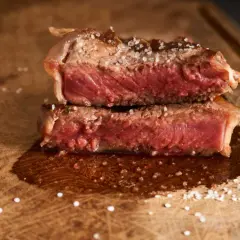 Filet mignon coupé en deux, saignant et parsemé de gros sel sur une planche en bois. Parfait pour une recette filet mignon moelleux.