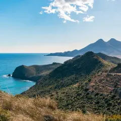 Paisaje costero en Cabo de Gata, con el mar azul intenso y montañas verdes.