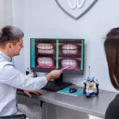 Stomatolog pokazuje pacjentce zdjęcia uśmiechów na monitorze.
