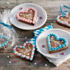 Bunte Lebkuchenherzen selber machen: mit Zuckerguss und Sprüchen verziert, liegen sie auf Holztisch.