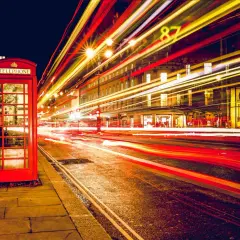 Klasyczna czerwona budka telefoniczna na tle nocnej ulicy z rozmazanymi światłami samochodów, efekt długi czas naswietlania zdjecia.