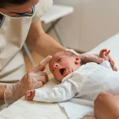 Niemowlę staje na głowie, gdy fizjoterapeuta delikatnie dotyka jego czoła. Maluch z otwartymi ustami wygląda na zaskoczonego.