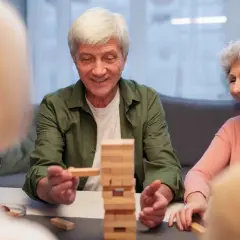 Un homme âgé retire une pièce d'un jeu Jenga, un exemple de stimulation cognitive pour personnes âgées.
