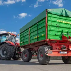 Czerwony traktor ciągnie zieloną przyczepę z plandeką. Duża masa przyczepy gotowa do pracy na polu.